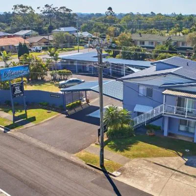 An elevated daytime view of the two-story 'Almare Tourist Motel' complex, painted pale blue with a dark blue roof, situated on a street corner in a suburban area.