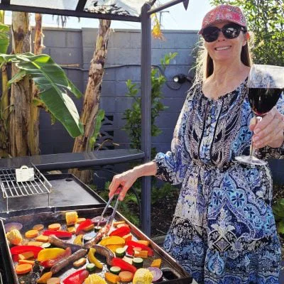 smiling woman with a pink cap and sunglasses is cooking colourful vegetables